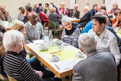 Saal, Begegnung, jeweils etwa sechs Personen an Tischen im Gespräch