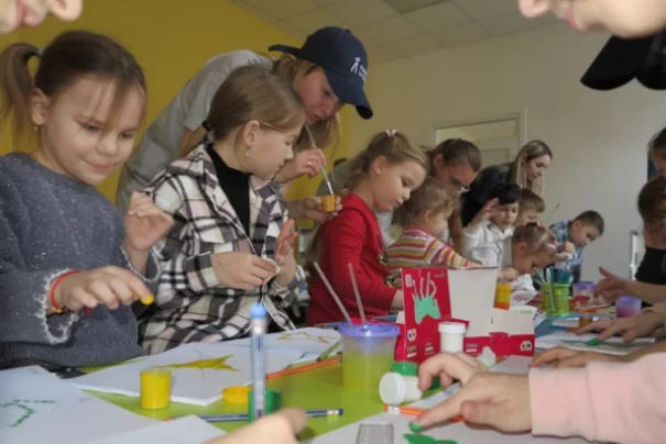 Mehrere Kinder malen mit Fingerfarben, unterstützt von Betreuern.
