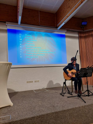 Ein Mann sitzt auf dere Bühne und spielt Gitarre.